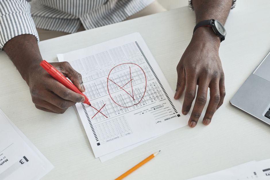 Close-up of a teacher marking a test paper with a red marker on a desk.